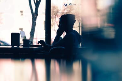 Silhouette of a person sitting in a coffee shop with a laptop
