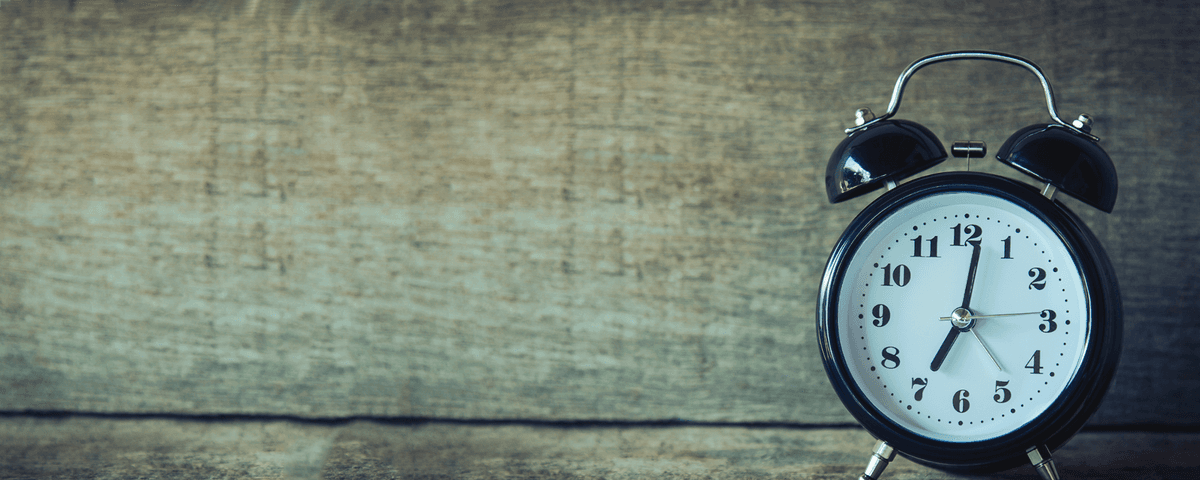 Close-up of a vintage-style black alarm clock with a white clock face, black numerals, and twin bells on top, set against a rustic wooden background.